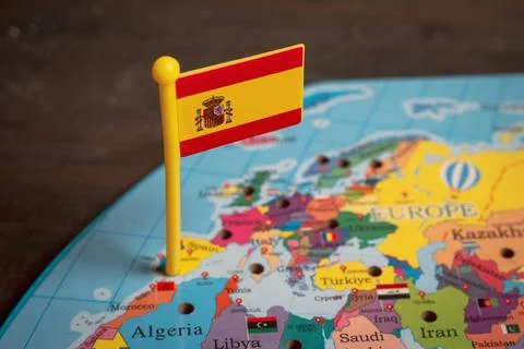 Small Spanish flag push pin on a colorful world map Stock Photos