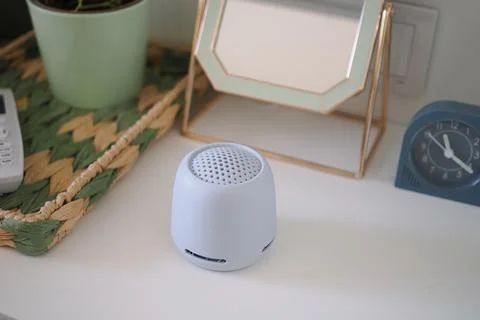 Small speaker placed on a table near a clock and a plant in a bright room Photos