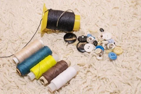 Small spools of thread of different colors and a bunch of buttons lie on a wh Stock Photos