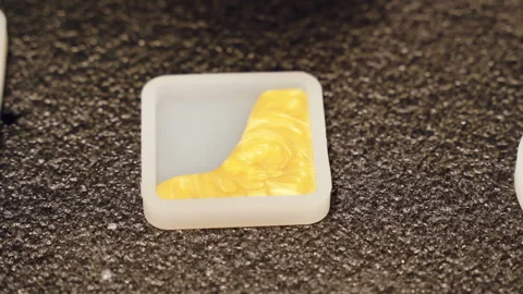 Small square silicone mold being filled with yellow and blue epoxy resin to Stock Footage 263192669