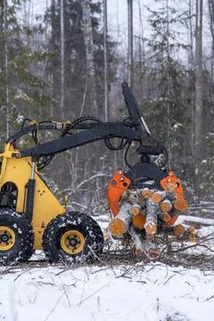 Small stand-on mini skid steer with grapple full of wooden logs Stock Photos