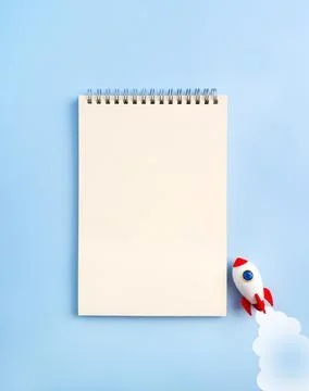 Small startup rocket flying near blank vertical notepad isolated on blue ba.. Stock Photos