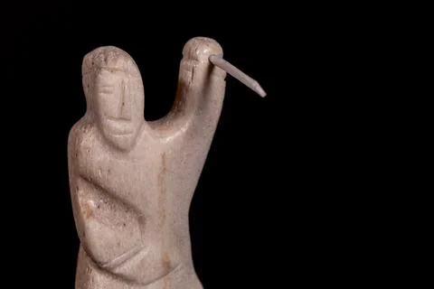 Small statue of Inuit hunter with a spear made of animal bone. Isolated on black Stock Photos