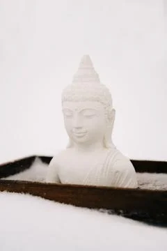A small statue of a white Buddha made of plaster on a wooden stand covered wi Stock Photos