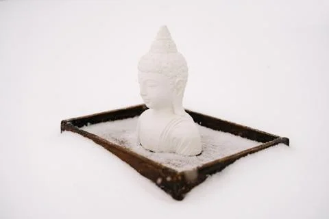 A small statue of a white Buddha made of plaster on a wooden stand covered wi Stock Photos