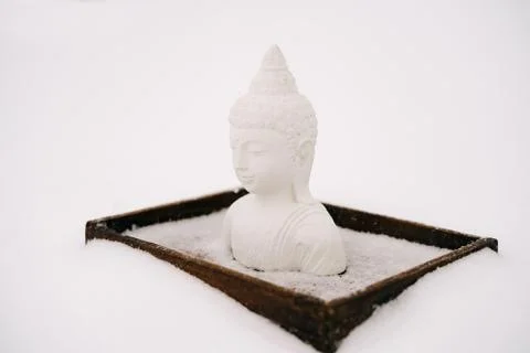 A small statue of a white Buddha made of plaster on a wooden stand covered wi Stock Photos