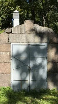 Small stone cellar structure with closed gray metal doors and a white vent Stock Photos