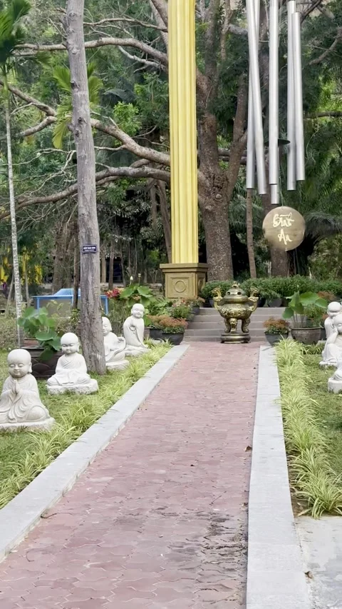 Small stone sculptures of buddha sit on the grass next to a paved walkway s.. Stock Footage 339444320