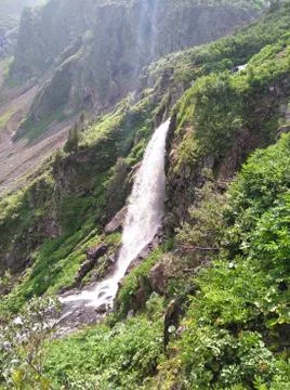 A small, stormy waterfall flowing down from sheer cliffs into a valley surrou Stock Photos