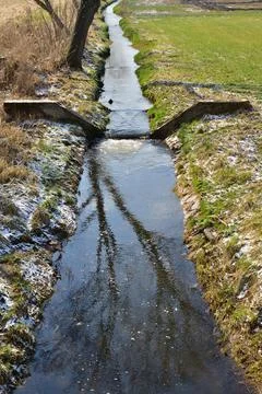 A small stream divided by a concrete dam, a sunny spring day. Stock Photos