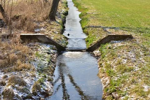 A small stream divided by a concrete dam, a sunny spring day. Stock Photos