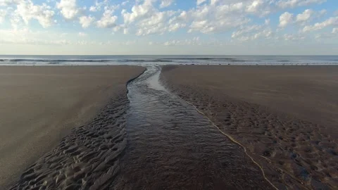 Small stream flowing on the beach into the ocean under cloudy sky. 4K Stock Footage 308420952