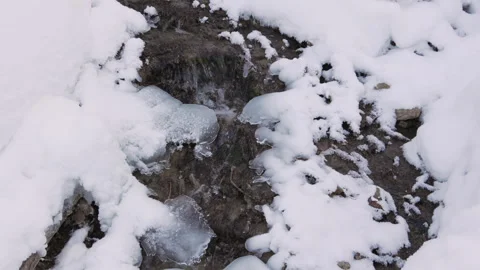 A small stream flowing through a snowy landscape, banks iced over. 動画素材 327713030
