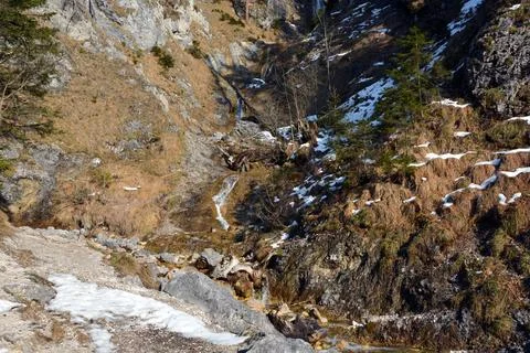 A small stream flows along the stony slope of the winter mountain Stock Photos