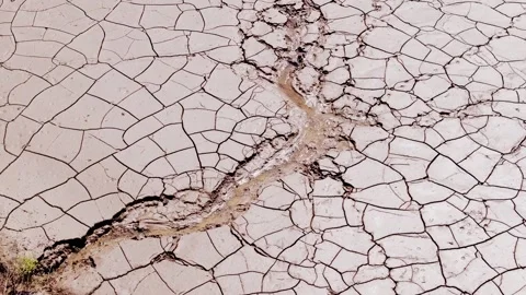 Small Stream Flows Through Cracked Earth as Sun Reflects in Dry Valley, 4K Video stock 310668024