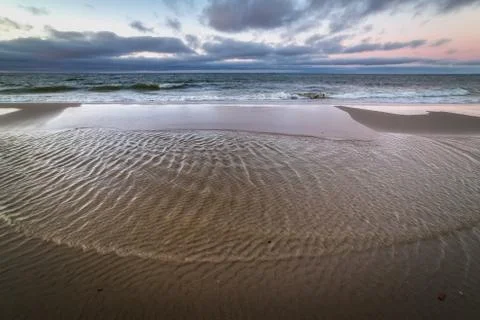Small stream flows into the waters of the Baltic sea at sunset Stock Photos
