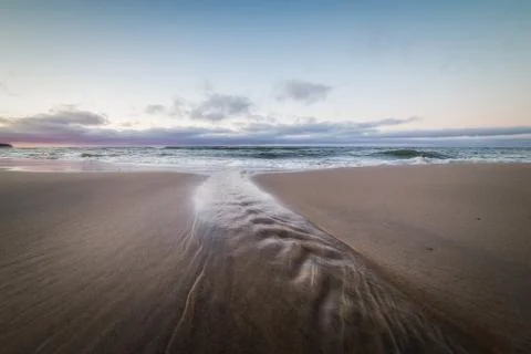 Small stream flows into the waters of the Baltic sea at sunset Stock Photos