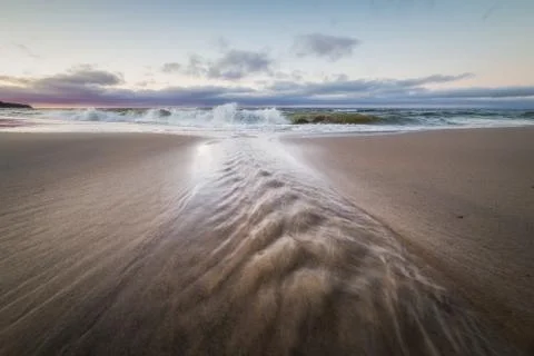 Small stream flows into the waters of the Baltic sea at sunset Stock Photos