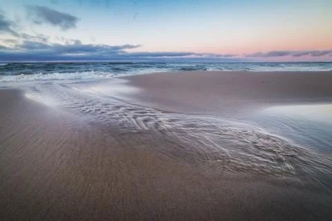 Small stream flows into the waters of the Baltic sea at sunset Stock Photos