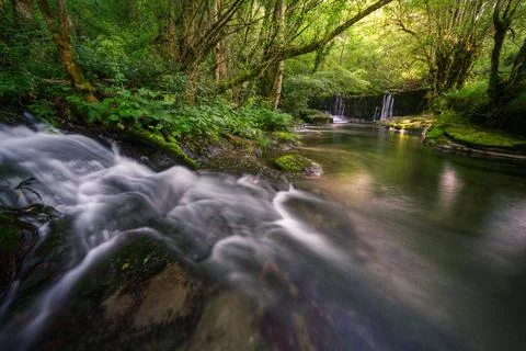 A small stream flows into a wide pool under a dam Stock Photos