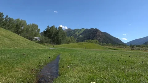 Small stream runs through a large green lawn.  Man walks by. 動画素材 117187020