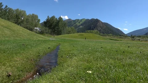 Small stream runs through a large green lawn. Cyclist rides by on path￼. Stock Footage 117187611