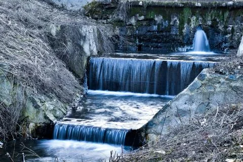 Small stream with watterfalls exiting old dam Stock Photos