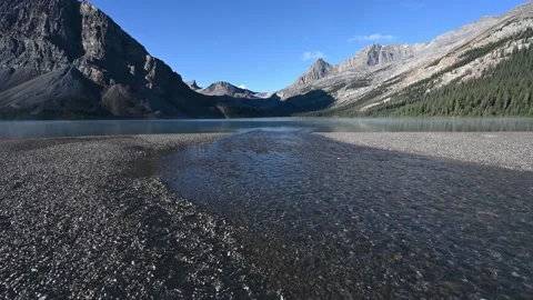A small streams with multicolored pebbles and mountain and blue sky in backgroun Stock Footage 295077434