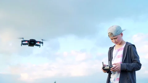 Small stylish boy in a cap launches a drone into the sky outside.  Stock Footage 138601512