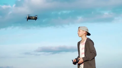 Small stylish boy in a cap launches a drone into the sky outside.  Stock Footage 138601603
