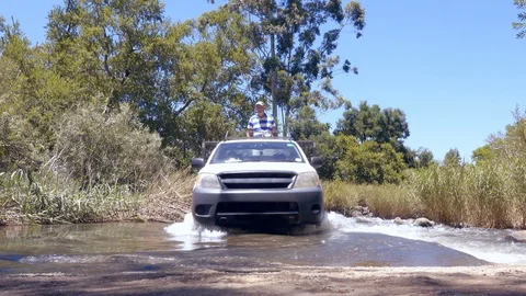 Small SUV crossing flooded bridge with farmer riding on the back South Africa Stock Footage 87574434