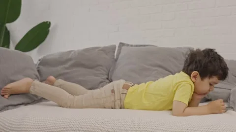 Small sweet kid relaxing on sofa using learning application on cellphone Stock Footage 245677346