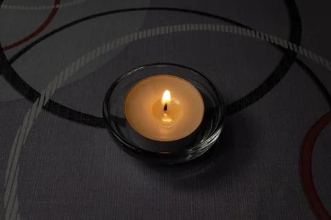 Small tea light candle burning in a glass holder on a textured dark backgro.. Stock Photos