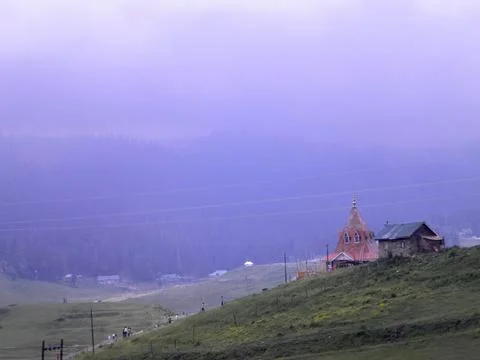 A small temple and a tiny house on top of a hill with dusty sky and pine trees Stock Photos