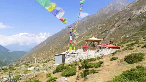Small temple at the slope surrounded by huge mountains and prayer buntings Stock Footage 77449824