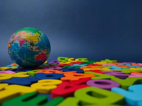 Small terrestrial globe ball rests among colorful wooden letters against a .. Stock Photos