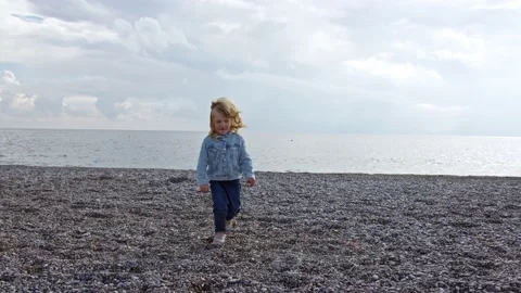 Small three-year-old child run away from cold sea on camera along stone beach in Stock Footage 227051620