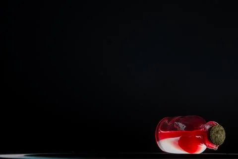 Small tiny bottle with red liqiud lying down black background Stock Photos