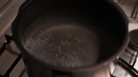 Small tiny bubbles forming on surface of water as heats in pot on stove Stock Footage 291466126