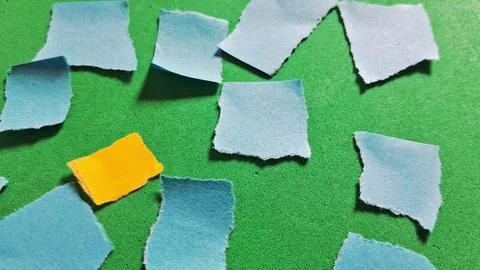 Small torn blue paper scraps scattered on a bright green surface Stock Photos
