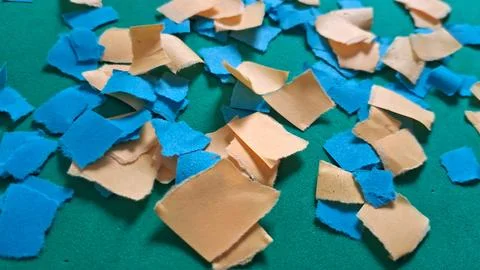 Small torn pieces of blue and yellow paper on green background Stock Photos