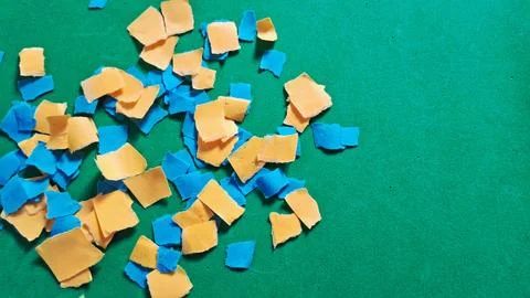 Small torn pieces of blue and yellow paper on green background Stockfoto's