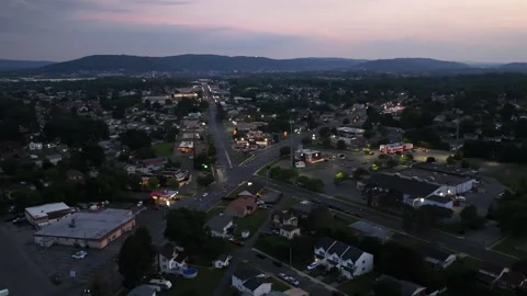 Small town intersection glows with illuminated signs and streetlights, houses Stock Footage 340970889