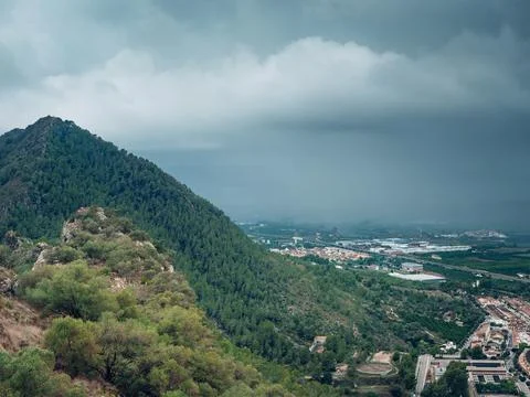 A small town under a mountain to which heavy rain and storm clouds is moving Stock Photos