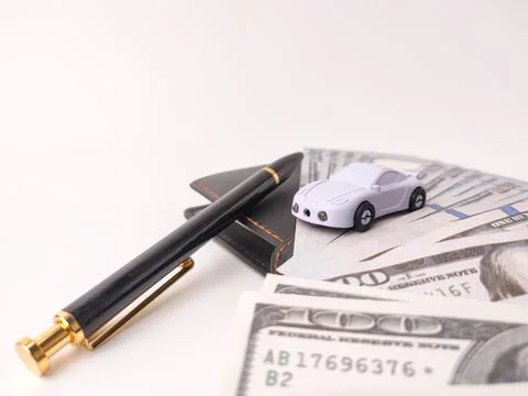 Small toy car model resting on top of US dollar bills and a pen, likely sym.. Stock Photos