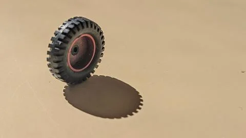 Small toy wheel casting a long shadow on a beige surface Stock Photos