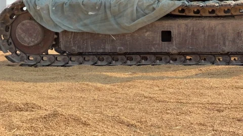 A small tracked tractor drives across drying rice on an open surface, assisting 스톡 동영상 338000819