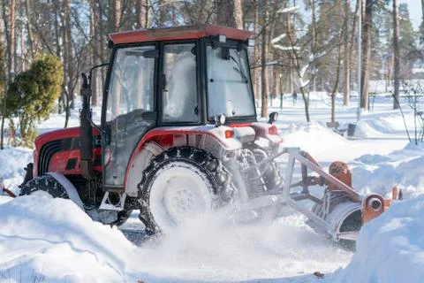 A small tractor with a rotating brush clears a wide road in the city park fro Stock Photos