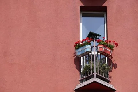 Small triangular balcony in the house with a coral facade and potted flowers  Stock Photos