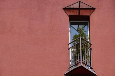 Small triangular balcony in the house with a coral facade and potted flowers  Stock Photos